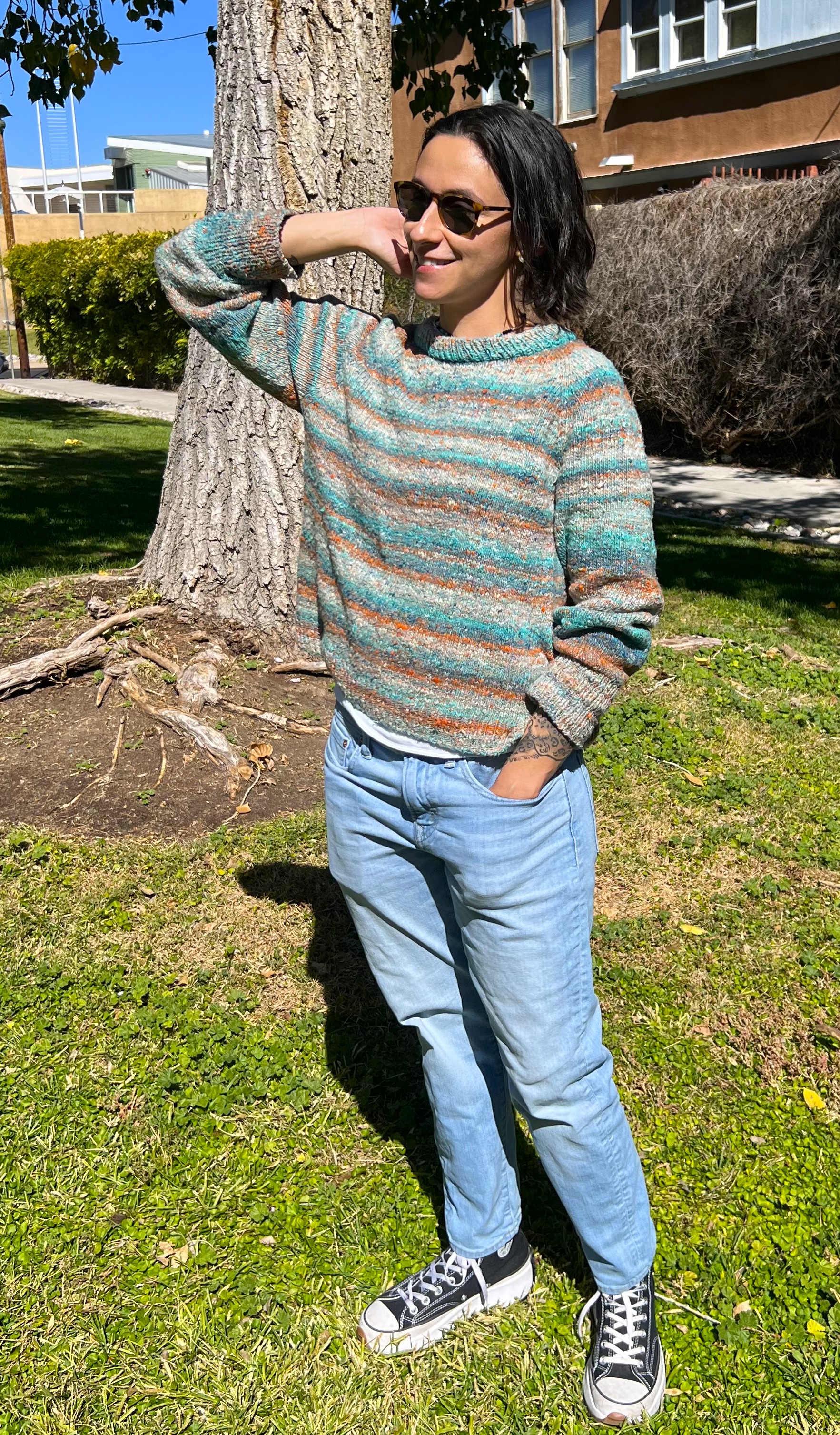 me standing in a park wearing the first sweater I ever knit, a variegated turquoise, white, and orange crew neck