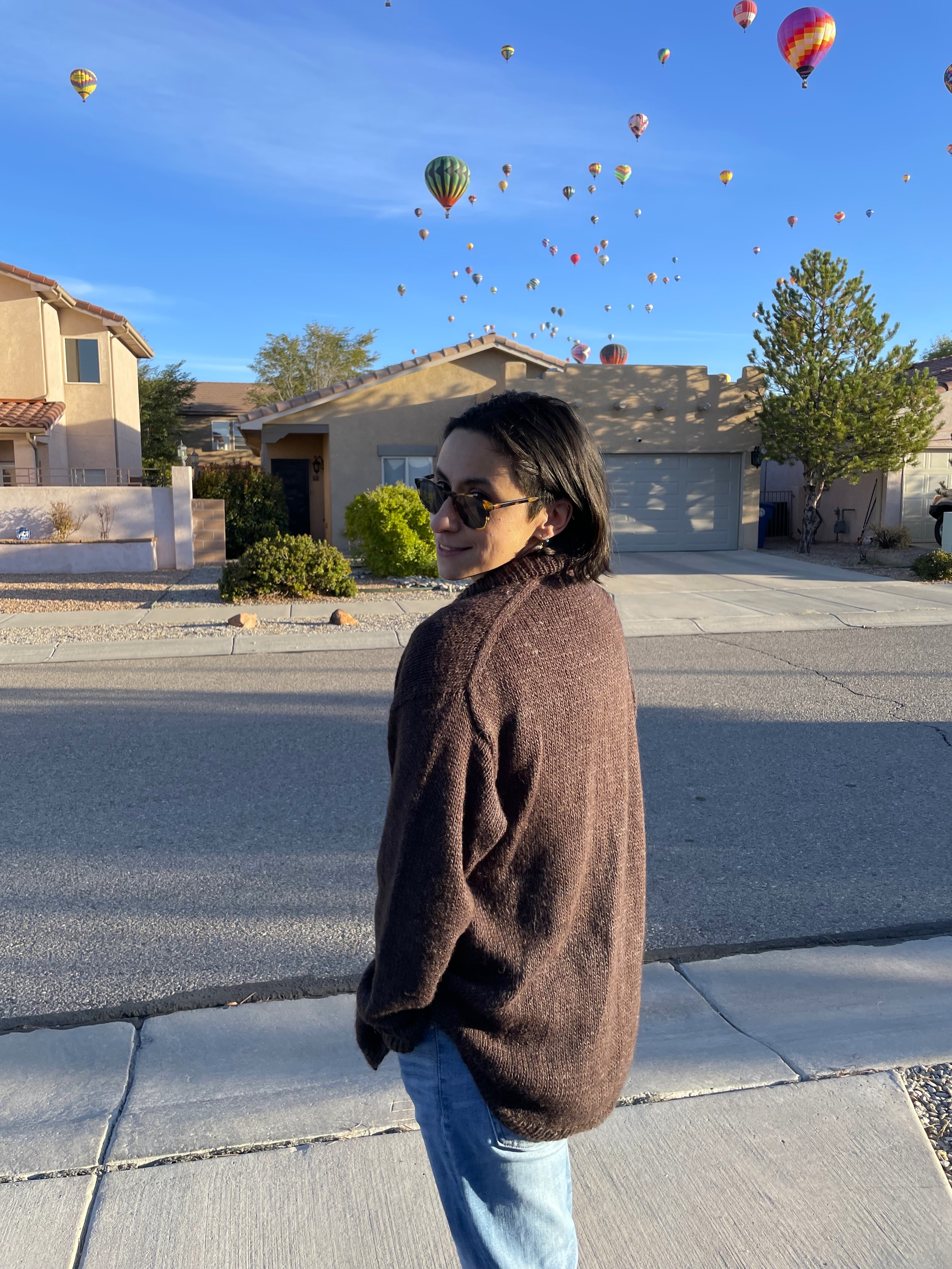 me wearing a brown knit shirt jacket with balloons from balloon fiesta in the background