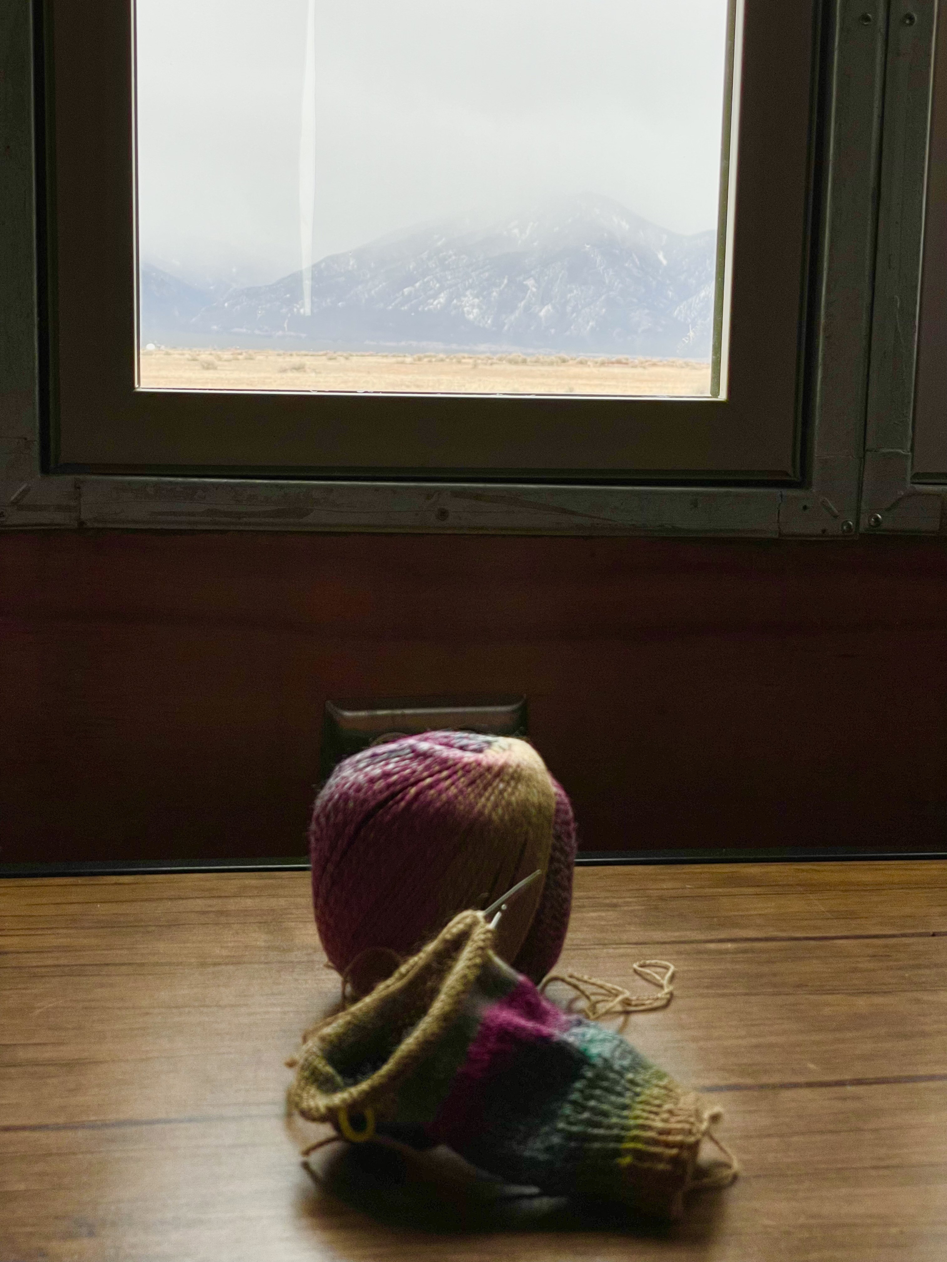 the leg of a sock on circular needles on top of a table with the snowy Taos mountains in the window view